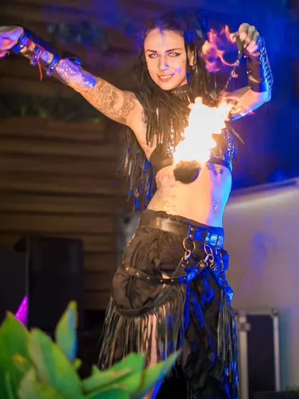 A female fire performer in a warrior-style costume strikes a powerful pose with her fire torches. This highlights the strong character work and costuming in our shows.