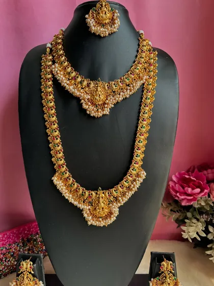 A complete temple bridal set with a choker, long necklace, earrings, and maang tikka. The design features Goddess Lakshmi motifs and is embellished with pearls.