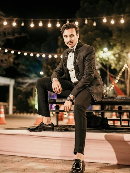 A dapper groom posing at night, with beautiful string lights creating a warm and festive background.