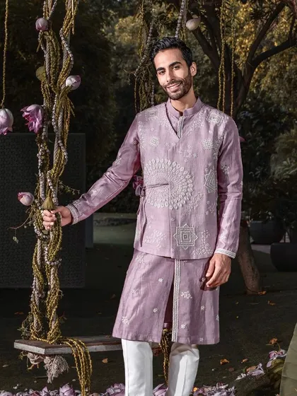 A smiling model wears the contemporary mauve kurta set, featuring an embroidered, overlapping panel. This ensemble radiates grace and grandeur for any celebration.