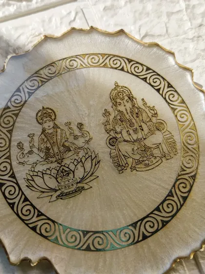 This elegant Laxmi Ganesh frame features intricate gold illustrations on a pearlescent white background. It's a beautiful piece for your home puja space or as a sophisticated festive gift.