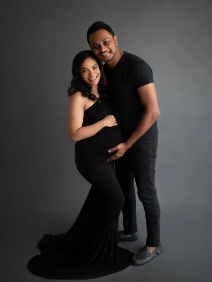 A happy couple portrait against a simple grey backdrop. Their coordinated black outfits create a chic and modern look for their maternity session.