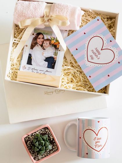 A Mother's Day gift set featuring a custom mug, a succulent plant, a personalized photo stand, and a soft towel.