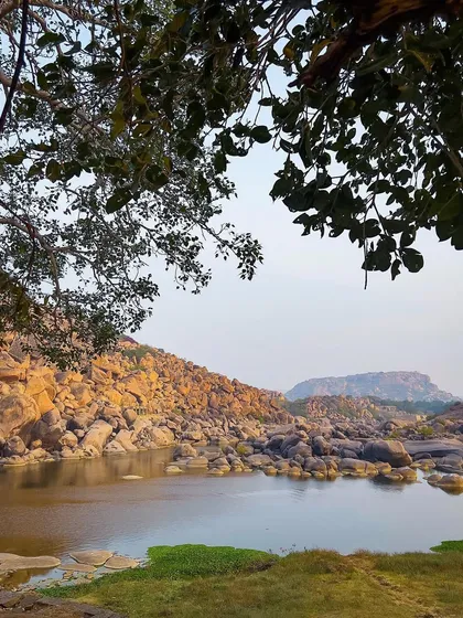 A view of the river and rocky terrain, framed by the leaves of a tree. This photograph captures the natural beauty of Hampi beyond just its temples and ruins.