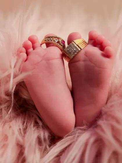 A creative and symbolic shot of a newborn's feet adorned with their parents' wedding rings, signifying the new family bond.