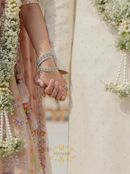 A close-up shot of the couple holding hands, a simple yet powerful symbol of their union. The details of their outfits and the floral garlands are beautifully captured.