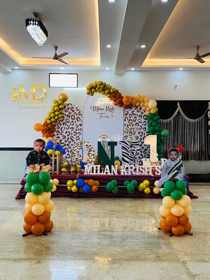 A wide shot of the complete jungle-themed stage, featuring animal print backdrops, a multi-colored balloon arch, and custom cutouts of the birthday boy.