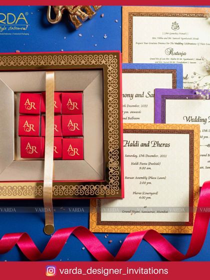 This invitation box combines tradition with a sweet touch. It features a set of personalized chocolates with the couple's initials, presented alongside a full suite of colorful wedding cards with intricate borders.