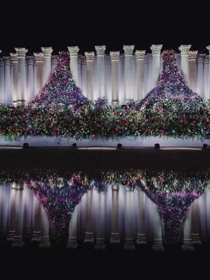 The reflection of the Roman pillars and floral mountains in the water creates a perfectly symmetrical and artistic visual, doubling the impact of the grand design.
