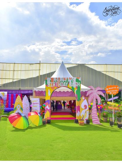 A wide shot of the grand entrance to 'Naavya's Birthday Bash'. The colourful archway, custom props, and large tent create an impressive welcome for guests.