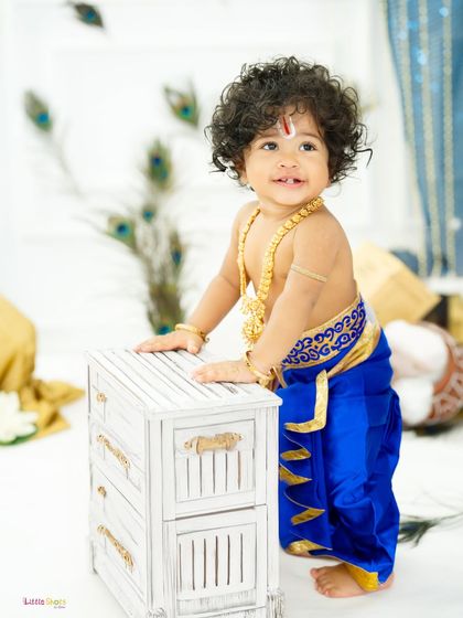 A playful little Krishna standing and exploring the studio set. His curious expression and adorable costume are the highlights of this Janmashtami photo.