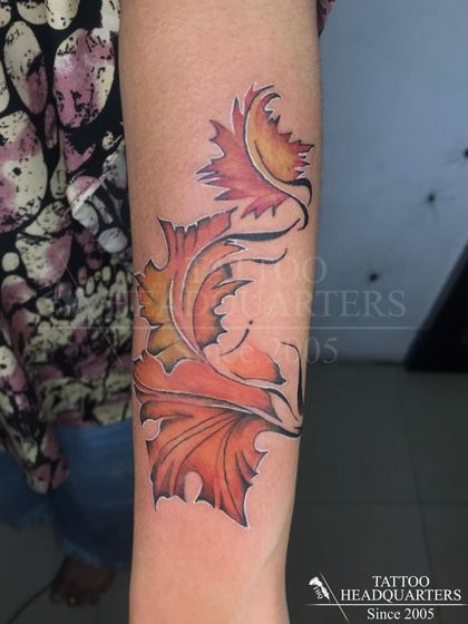 A vibrant tattoo of autumn leaves in shades of orange and yellow, appearing to swirl around the arm.