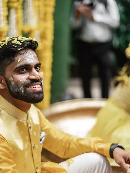 The groom, smiling, covered in a light dusting of haldi and flowers.