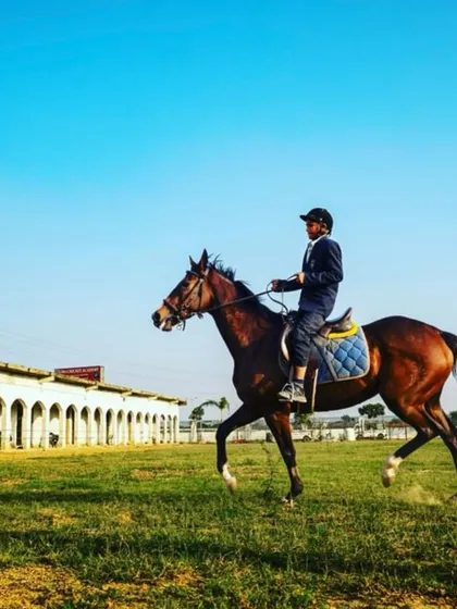 A student enjoys a ride on our expansive grounds, with our clean and professional stables visible in the background.