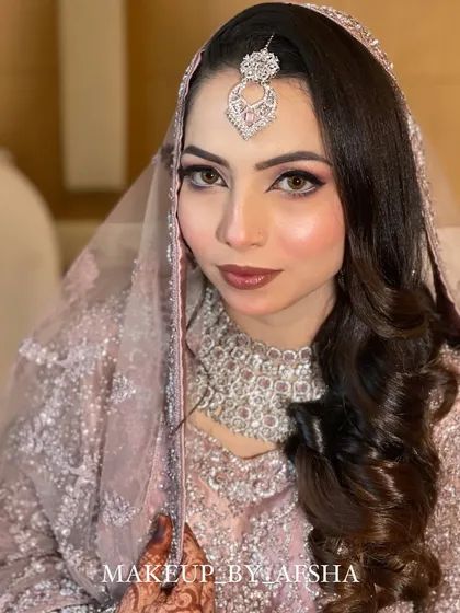 A stunning Walima look in a pastel pink dress with intricate silver work. The makeup is soft and luminous, with a focus on her beautiful eyes.