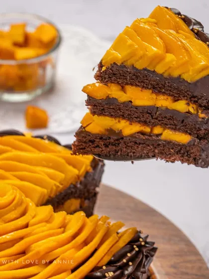 A perfect slice of my Belgian Chocolate Mango Cake. You can see the layers of moist chocolate sponge, rich ganache, and fresh mango pieces, all topped with an elegant mango rose.