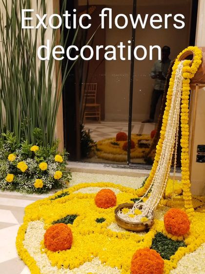 A traditional floor decoration, or rangoli, made with marigold petals. A brass pot overflowing with floral strings adds a classic and auspicious element to the design.