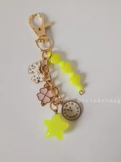 Here is the sunny yellow charm keychain, featuring a polka-dot bow, a four-leaf clover, a clock, and a star. It's a bright and cheerful accessory.
