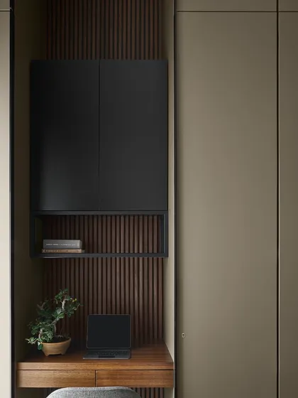 This compact study nook is built into the Taupe Bedroom, featuring a fluted wood backdrop and a matte black overhead cabinet. The design provides functional workspace and storage while maintaining the room's serene and cohesive feel.