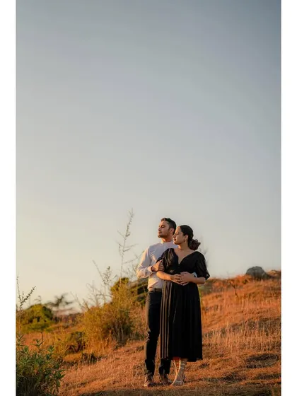 A wide portrait of a couple standing on a hillside during the golden hour, looking out at the view, capturing a moment of shared peace and reflection.