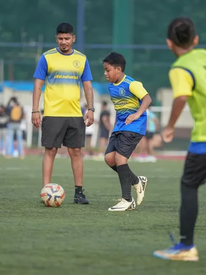 A coach observes a young player's technique closely during a drill. This image embodies our belief that behind every confident young player is a coach who believed in them first.