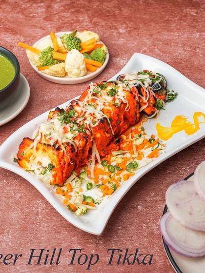 For our vegetarian guests, we have the Paneer Hill Top Tikka. Cubes of paneer are marinated, grilled, and topped with cheese, served with a side of green chutney.