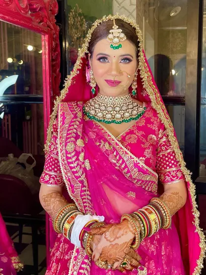 A stunning bride in pink. This look is all about radiance, with a glowing base and soft eye makeup that lets her beautiful green jewelry stand out.