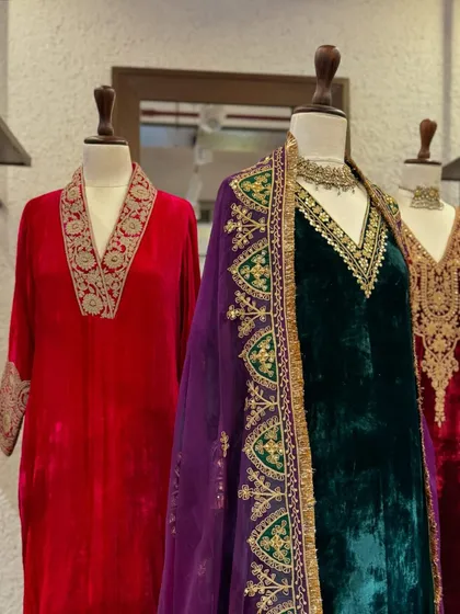 A close-up on the contrast between the bright red and deep emerald velvets, both adorned with intricate gold zardozi work.