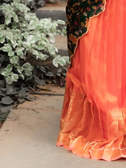 A detail shot of the hem of the metallic orange pleated skirt, showing the rich texture and traditional golden border.