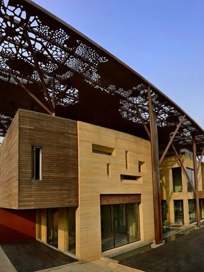 The Tree House facade is a blend of materials, including warm wood cladding and cool teakstone. The overhanging metal canopy provides shade and adds to the building's distinctive, layered appearance.