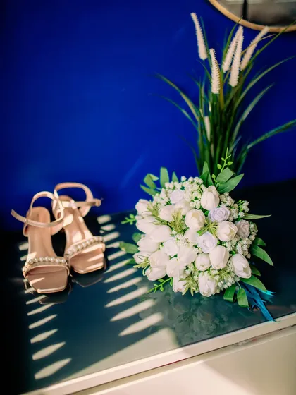 A beautifully styled flat lay of the bride's accessories, including her shoes and bouquet, captured in artistic light and shadow.