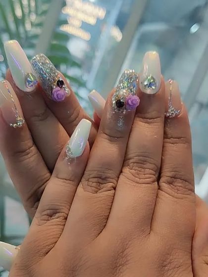 A beautiful white chrome set on long coffin nails, featuring accent nails with silver glitter, rhinestones, and charming 3D purple roses.