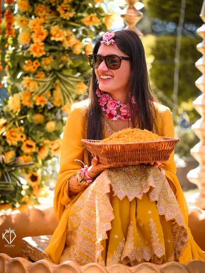 The bride, looking radiant in sunglasses and floral jewelry, holds a basket of marigold petals for the ceremony.