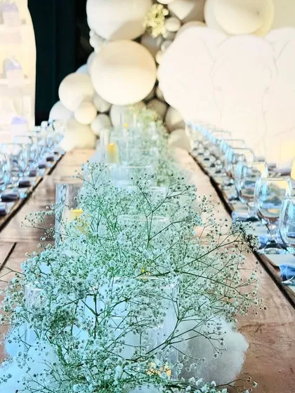 An exquisitely set dining table for a first birthday. The centerpiece is a runner of fluffy cotton and baby's breath, creating a dreamy, cloud-like effect.