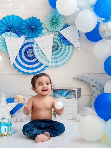 Surrounded by blue balloons, this happy one-year-old is having a wonderful time at his birthday-themed studio session.
