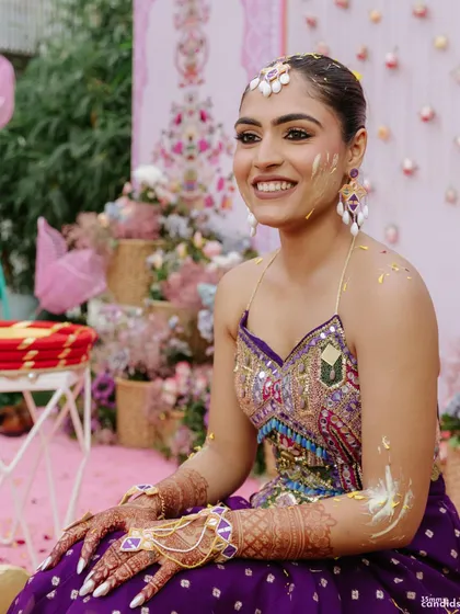 The bride's joyful expression after getting haldi applied, her sleek braid still looking perfect and keeping her hair out of the way.
