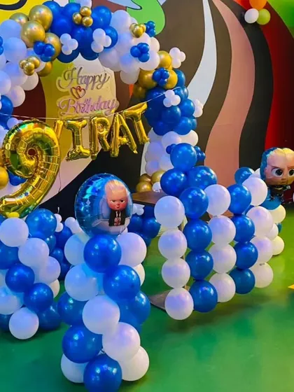 A cool Boss Baby themed birthday setup with a balloon arch and pillars in blue, white, and gold. The decoration includes a large number '9' foil balloon and the birthday boy's name, "Virat."