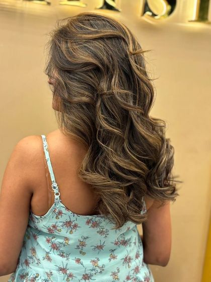 A side view of a client's new highlights, showing how the color cascades through her long hair. The soft waves add texture and showcase the different tones.