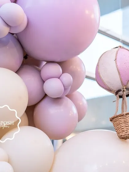 A miniature hot air balloon prop nestled among a cloud of pastel purple and cream balloons.