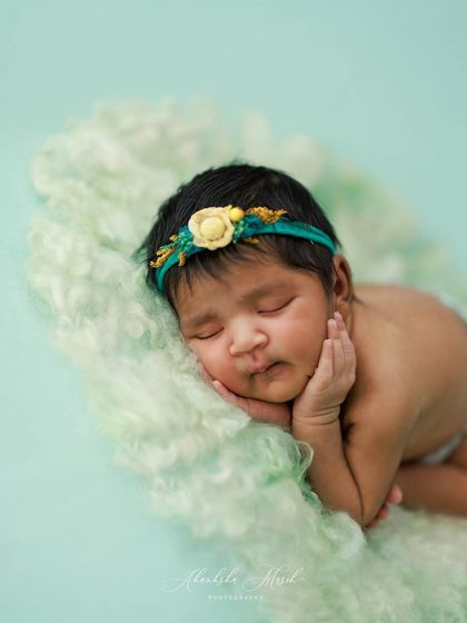 Just nine days old and already a natural. This classic "hands under chin" pose is perfect for showing off a newborn's delicate face, set against a soft mint green backdrop.