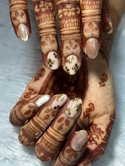 A beautiful engagement nail set. We used a shimmering champagne polish and a nude base with gold floral stickers to match her golden outfit and mehndi.