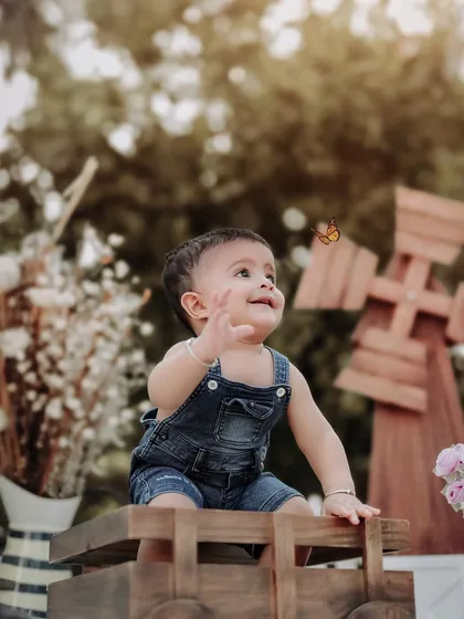 A moment of pure wonder as a butterfly flutters by. This outdoor setup with a wooden truck and windmill creates a charming, rustic scene for a little boy's photoshoot.