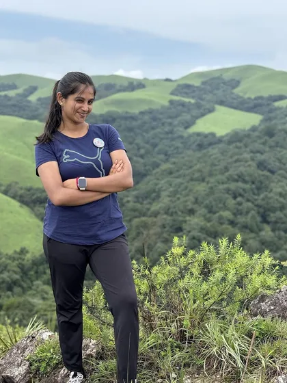 A trekker poses confidently on the trail, with the beautiful green hills of Bandaje behind her.