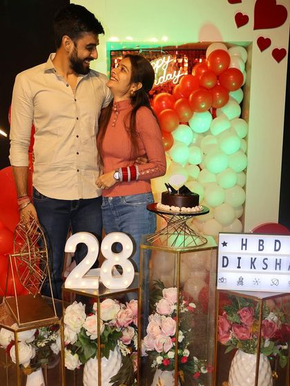 Posing for a photo amidst the beautiful birthday decorations. The "HBD DIKSHA" lightbox and the "28" marquee numbers add a personalized touch to her special day.
