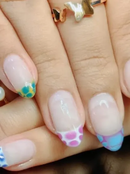 A fun and creative French manicure with colorful animal print-style spots on each tip, using shades of blue, orange, and pink.