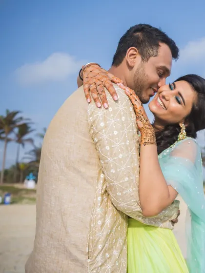 A close-up, joyful embrace between a couple on the beach. This candid shot perfectly captures the happiness and affection of a pre-wedding celebration, with the bride's mehendi adding a traditional touch.