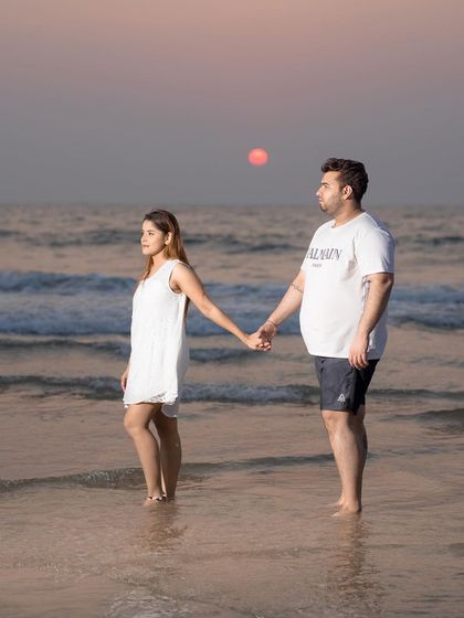 A serene pre-wedding photo of a couple holding hands on a Goan beach as the sun sets over the ocean. This image captures the quiet, romantic essence of a beach destination shoot.