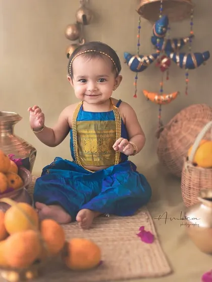 A happy baby girl surrounded by mangoes in a rustic, ethnic setup. Her smile and wave make this a wonderfully interactive and joyful portrait.