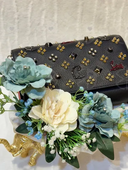 A stunning black studded handbag, presented with a bouquet of artificial blue and white flowers. The contrast creates a chic and modern look, perfect for a bride's accessory collection.
