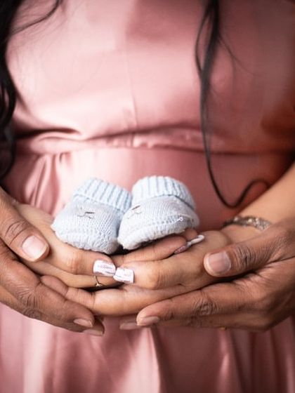 A close-up shot focusing on the hands of the parents-to-be, gently holding a tiny pair of baby shoes. It's a simple, powerful symbol of the little life they are waiting for.